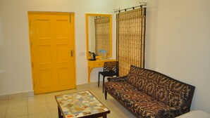 A room with a yellow door, a sofa, a small table, a desk with a chair, and a mirror. - Hotel Kabli (New Delhi)