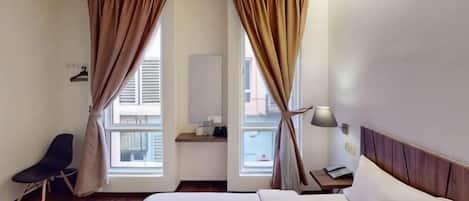 A hotel room with a bed, a chair, a nightstand, a lamp, and curtains.