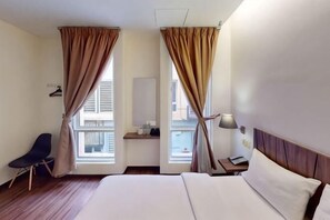Una habitación de hotel con cama, una silla, una mesita de noche, lámpara y cortinas.