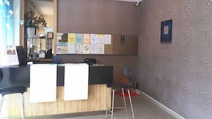 A reception area with a wooden counter, a bulletin board with notices, and a seating area with stools.