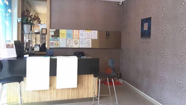 Un área de recepción con un mostrador de madera, un tablón de anuncios y un espacio de espera con taburetes.