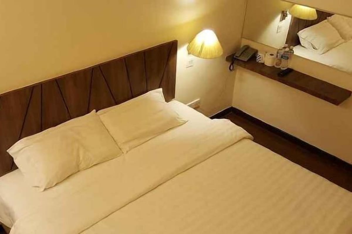 Een hotelkamer met een bed, nachtkastje, lamp, spiegel en een plank met toiletartikelen.