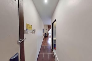 Un pasillo estrecho con una puerta a la izquierda, un letrero en la pared y una ventana al final.