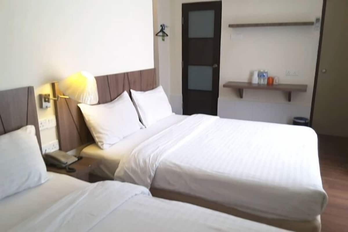 Habitación de hotel con dos camas individuales, una mesita de noche con lámpara, un teléfono y un pequeño estante con artículos de tocador.