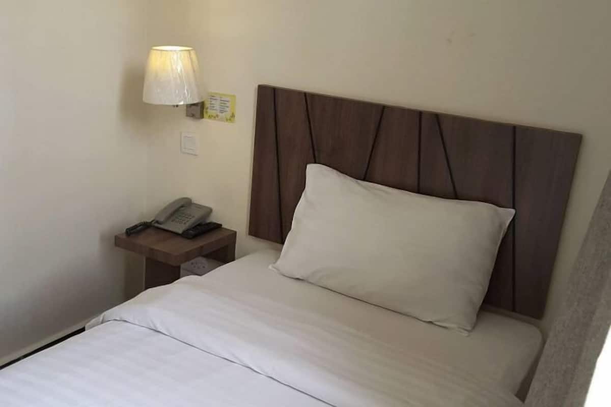 Una habitación de hotel con una cama, una mesita de noche con lámpara y un teléfono.