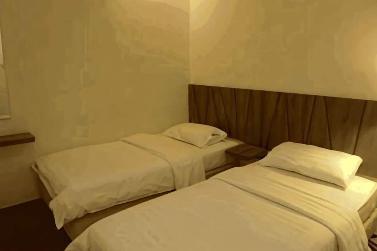 Una habitación de hotel con dos camas individuales, un cabecero de madera y una mesita de noche.