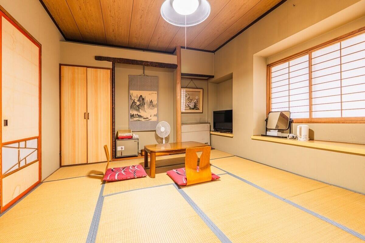 Une pièce de style japonais traditionnel, avec un sol recouvert de tatamis, une table basse, un éventail, un téléviseur et une porte coulissante.