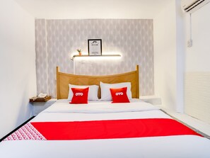 Quarto de hotel com uma cama, uma mesa de cabeceira, uma citação emoldurada na parede e um edredom vermelho e branco.