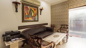 A living room with a sofa, a coffee table, a printer, an air conditioner, and a painting on the wall. - Red Maple Bed & Breakfast (New Delhi)