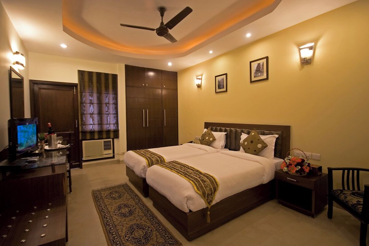 A hotel room with a large bed, a desk with a computer, a ceiling fan, and a nightstand with a lamp.