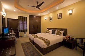 A hotel room with a large bed, a desk with a computer, a ceiling fan, and a nightstand with a lamp. - Red Maple Bed & Breakfast (New Delhi)
