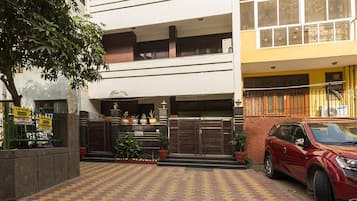A multi-story building with a gated entrance, potted plants, and a red car parked outside.