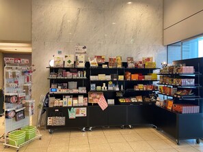 Ein Geschäft mit Regalen voller verschiedener Produkte, einem Auslagekarren mit grünen Körben und einem gefliesten Boden.