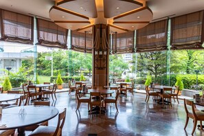 A spacious outdoor dining area with multiple tables and chairs, surrounded by large windows offering a view of greenery. - Hiroshima City Bunka Koryu Kaikan (Hiroshima)