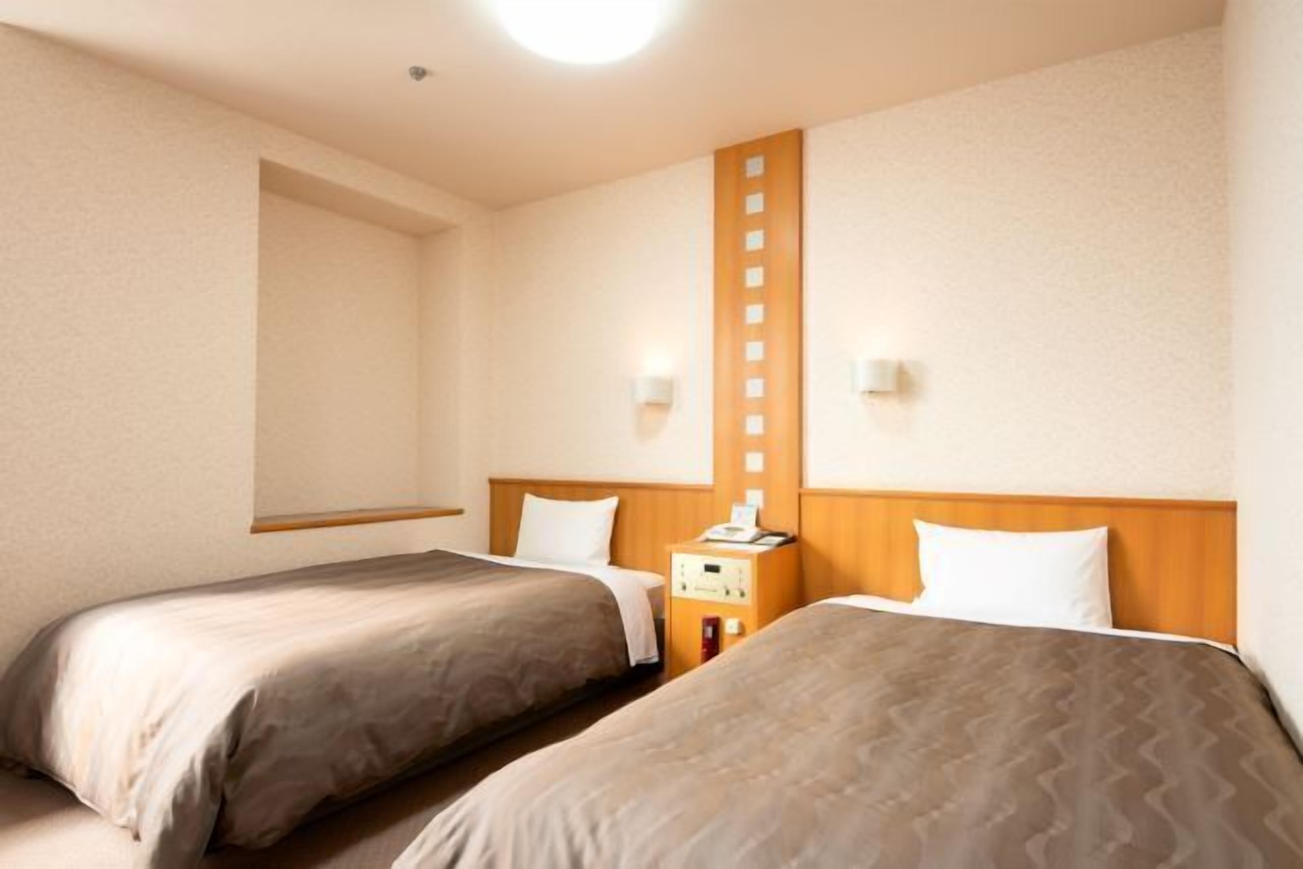 Ein Hotelzimmer mit zwei Betten, einem hölzernen Kopfteil, einem Nachttisch mit Lampe und einer Wandleuchte.