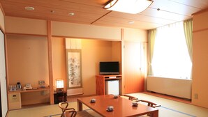 A traditional Japanese room with tatami flooring, a low table with cushions, a television, and a sliding door.