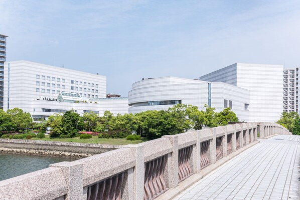 Un edificio moderno con fachada curva, un puente de piedra y una masa de agua al frente.