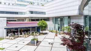 A modern building with a covered outdoor seating area, potted plants, and a clear sky.
