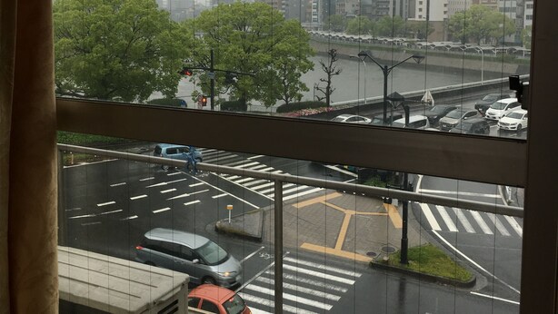 A view from a window overlooking a cityscape with buildings, a river, and a parking lot. - Tenryu Ryokan (Hiroshima)