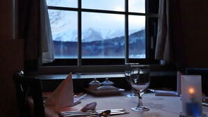 A table set for dining with a candle, a glass, and a view of snow-covered mountains through a window. - Tokachi Sahoro Resort (Shintoku)