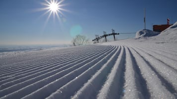 A snow-covered ski slope with ski tracks and a clear sky.