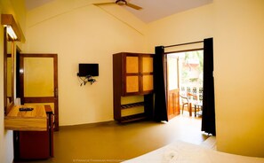 A room with a bed, a desk with a computer, a TV mounted on the wall, and an open door leading to an outdoor area with a table and chairs. - Lua Nova (Baga)