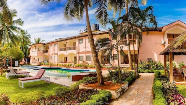 A resort with a swimming pool, palm trees, and a building with balconies. - Lua Nova (Baga)