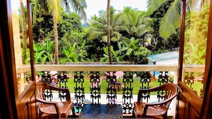 A balcony with two wooden chairs, a metal railing, and a view of lush greenery and a building in the background. - Lua Nova (Baga)
