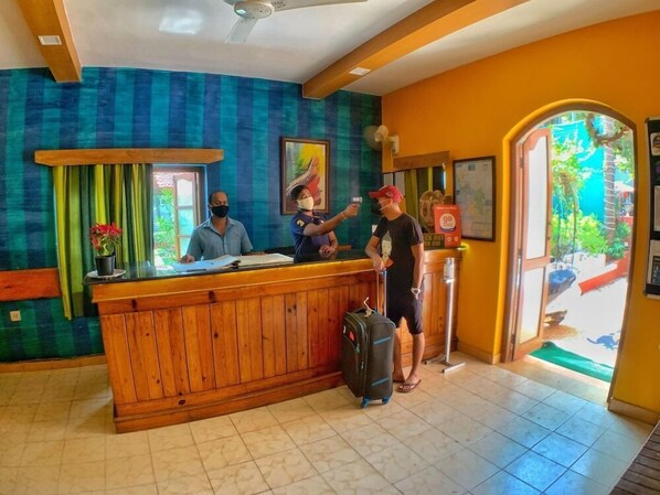 A reception desk with wooden paneling, a large window with green curtains, and a view of the outside. - Lua Nova (Baga)