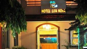 The entrance of Hotel Lua Nova with a neon sign, an arched doorway, and a view of the interior through the glass door. - Lua Nova (Baga)
