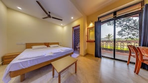 A bedroom with a bed, a bench, a ceiling fan, a bathroom with a patterned wall, and a balcony with a view of greenery. - Lua Nova (Baga)