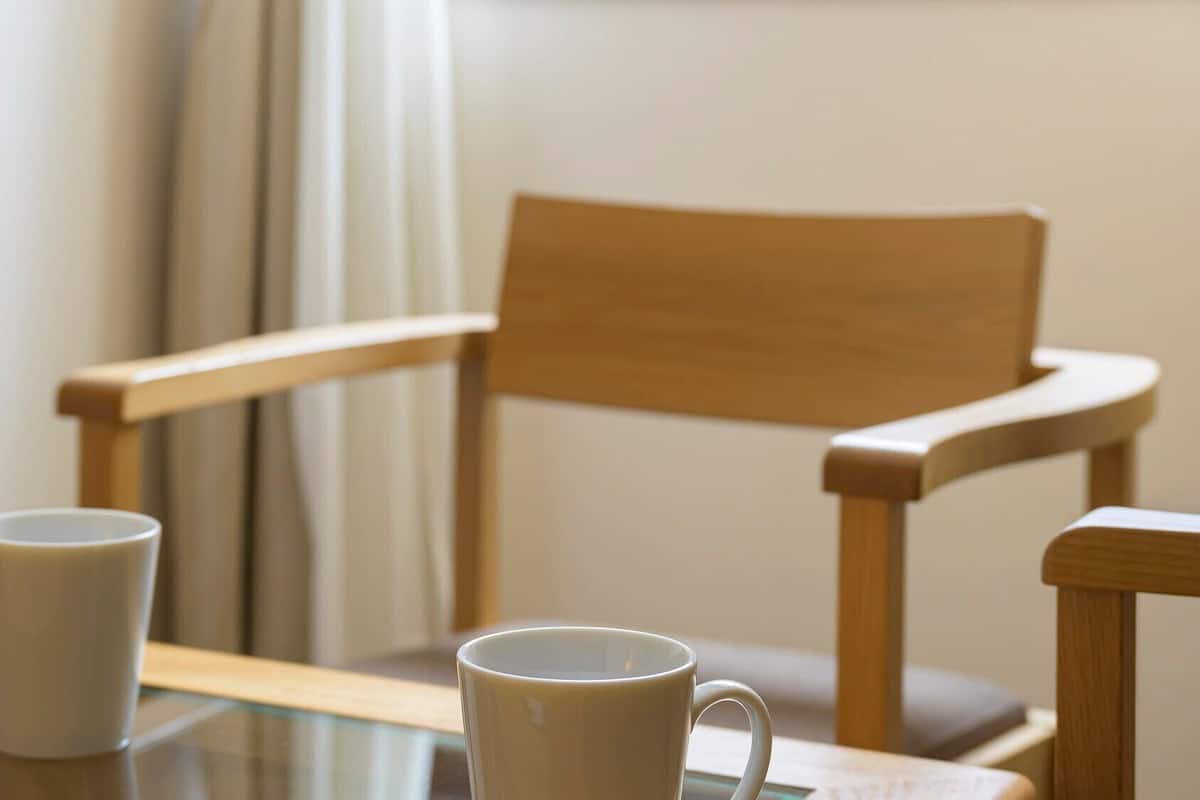 Une chaise en bois et deux tasses blanches sur une table en verre.