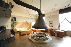 Ein moderner Lounge-Bereich mit einem zentralen Kamin, Sitzgelegenheiten und einem Fernseher an der Wand.