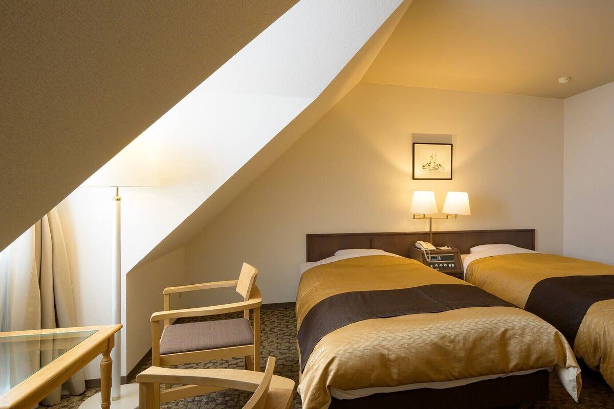 Une chambre d’hôtel avec deux lits, un bureau, une chaise et un tableau au mur.
