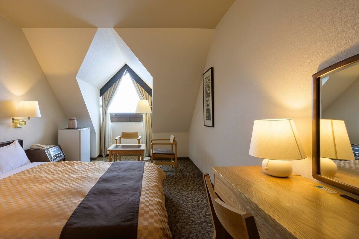 Une chambre d’hôtel équipée d’un lit, d’un bureau, d’une chaise, d’une lampe et d’un grand miroir.