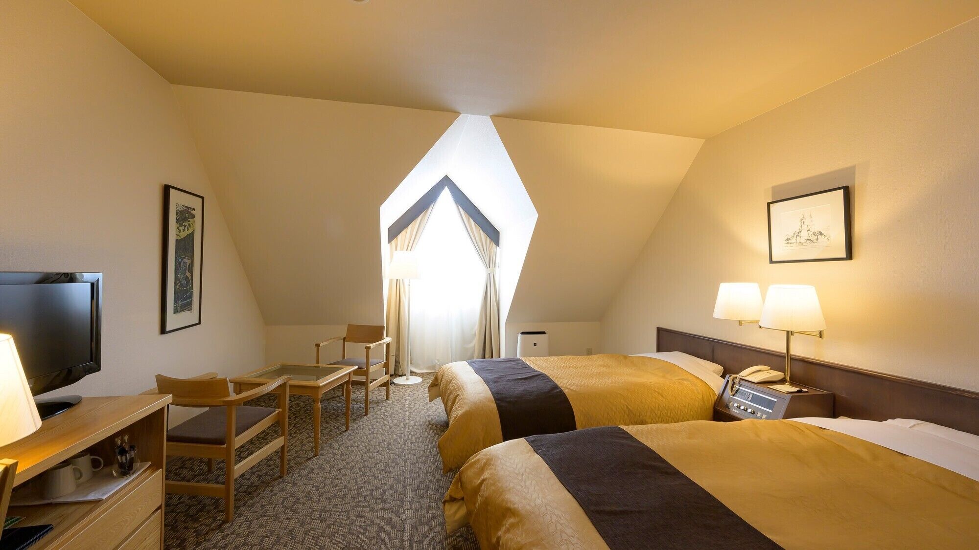 A hotel room with a television, desk, two beds, and a large window.