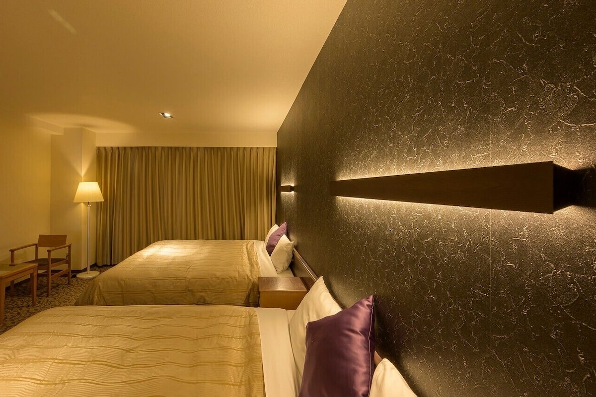 Une chambre d’hôtel avec deux lits, un bureau, une chaise, une lampe et un tableau encadré au mur.