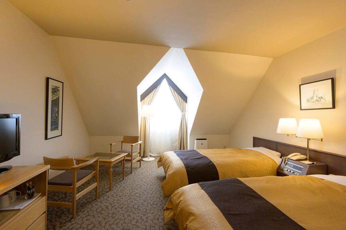 Une chambre d’hôtel avec deux lits, un bureau avec une chaise, une télévision et une grande fenêtre.