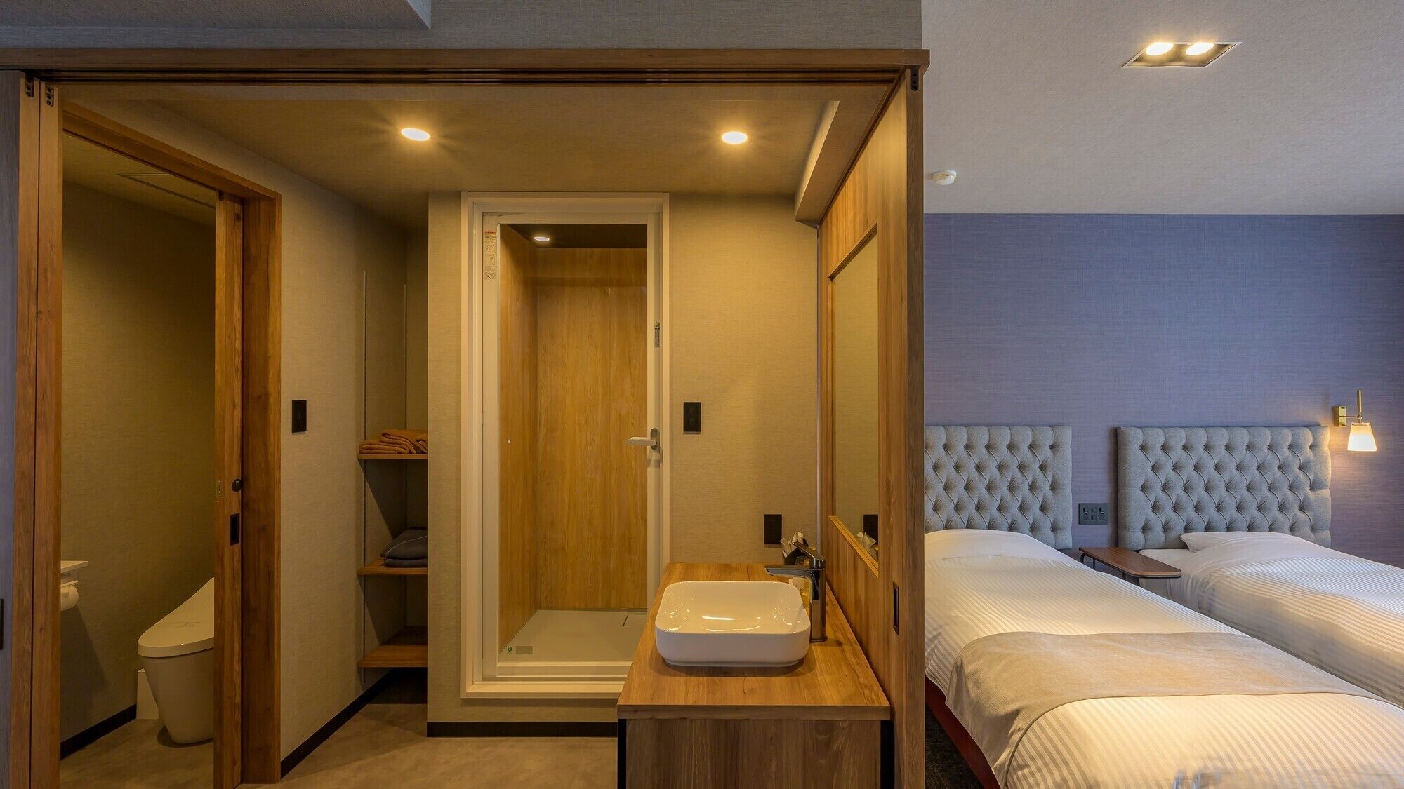 A hotel room with a shower, a sink, two beds, and a nightstand.