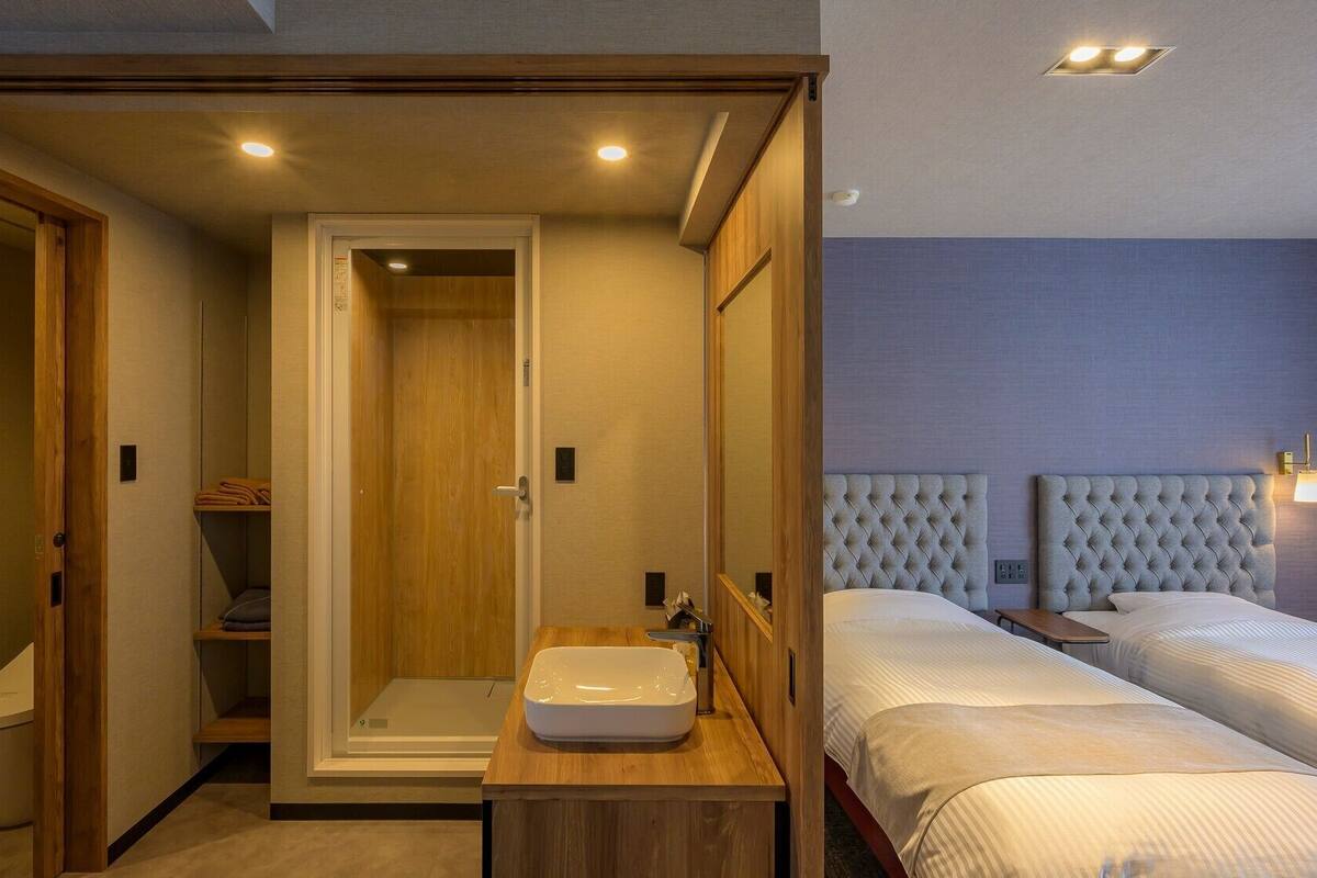 Une chambre d’hôtel avec un dressing, une douche, un lavabo et deux lits.
