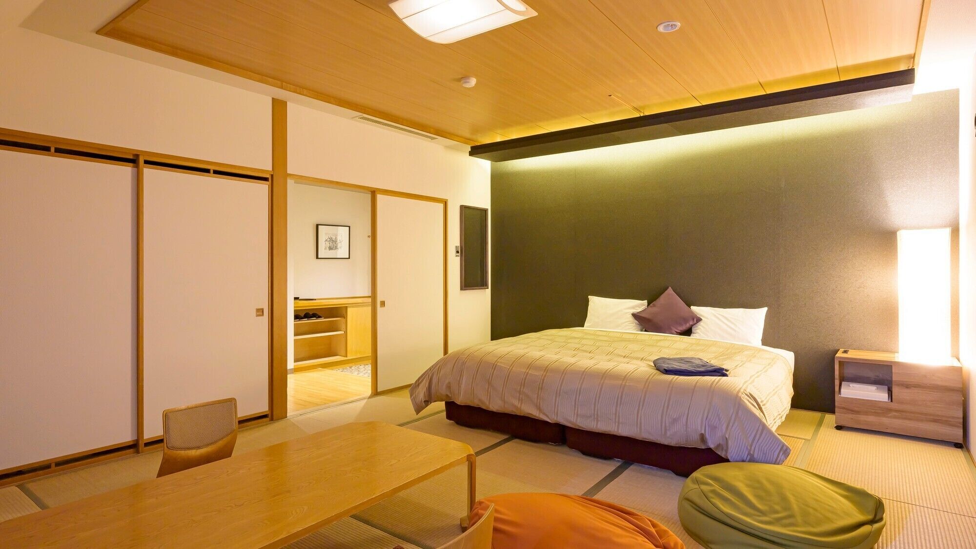 A hotel room with a bed, bedside table, chair, and a small table.