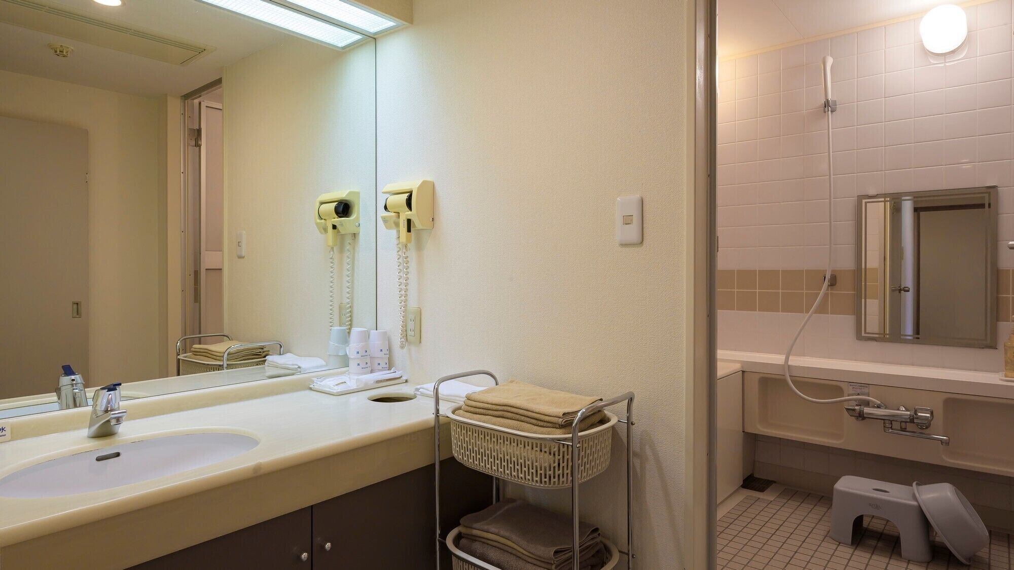 A hotel bathroom with two sinks, a mirror, a towel rack, a shower, and a toilet.