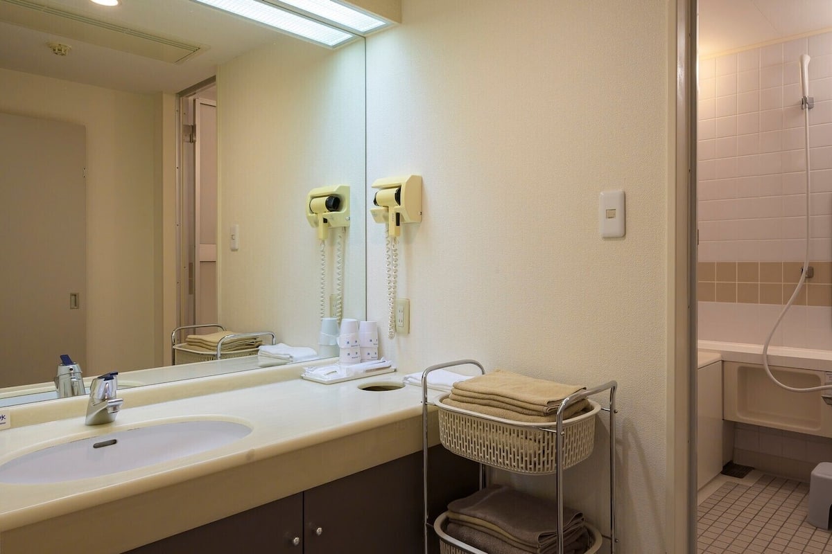Une salle de bain d’hôtel avec deux lavabos, un miroir, un porte-serviettes, une douche et des toilettes.