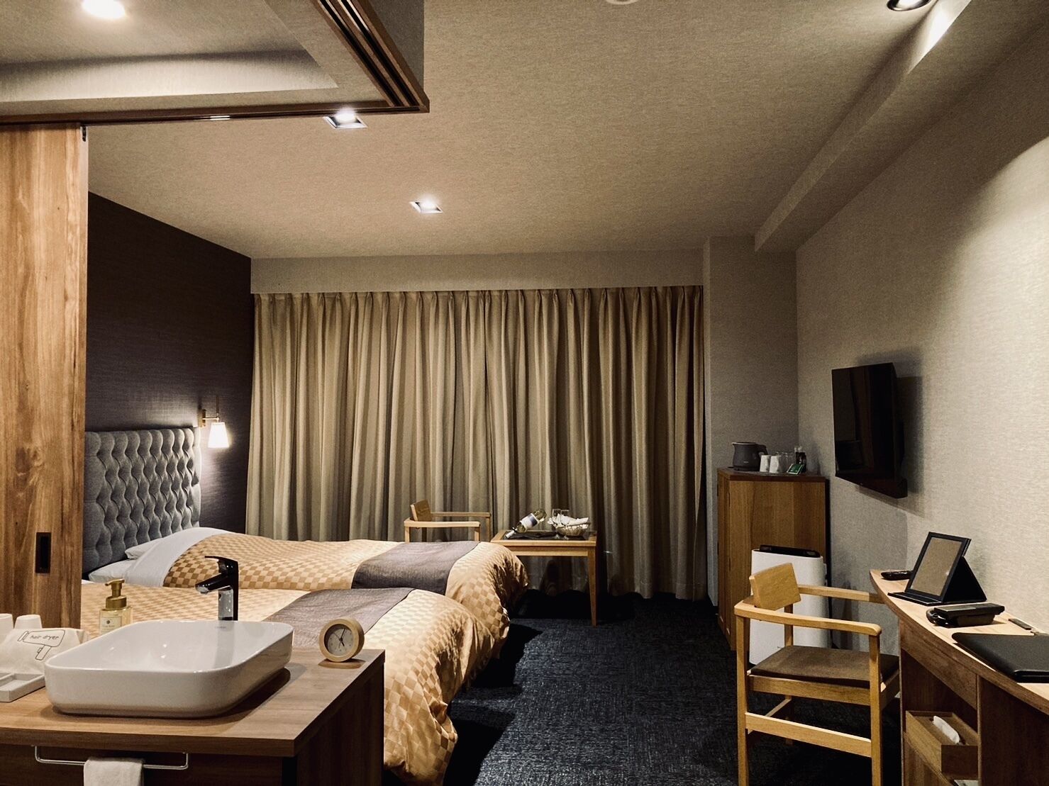 A hotel room with a bed, bedside table, desk, chair, TV, and curtains.