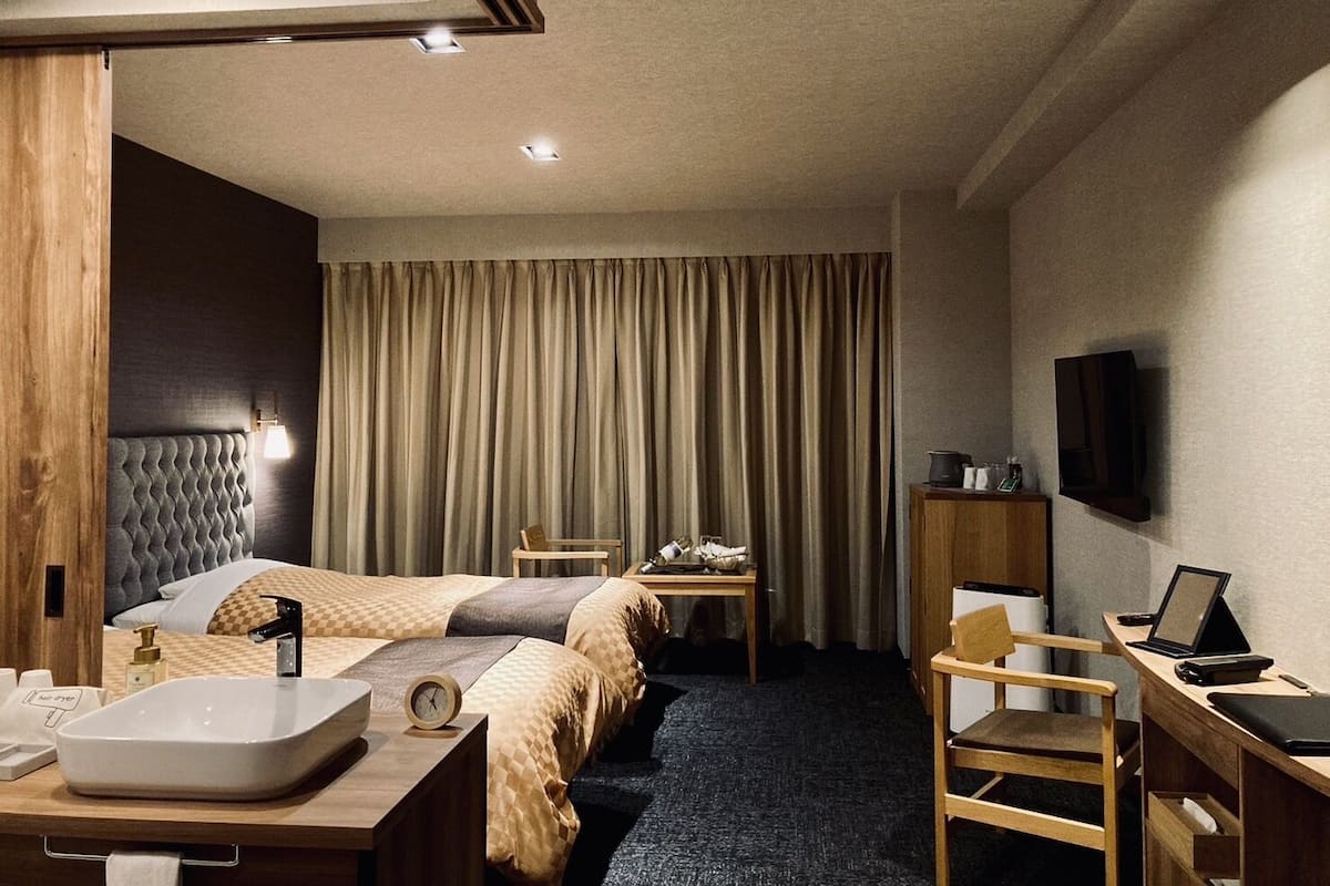 Une chambre d’hôtel comprenant un lit, une table de chevet, un bureau, une chaise, une télévision et des rideaux.