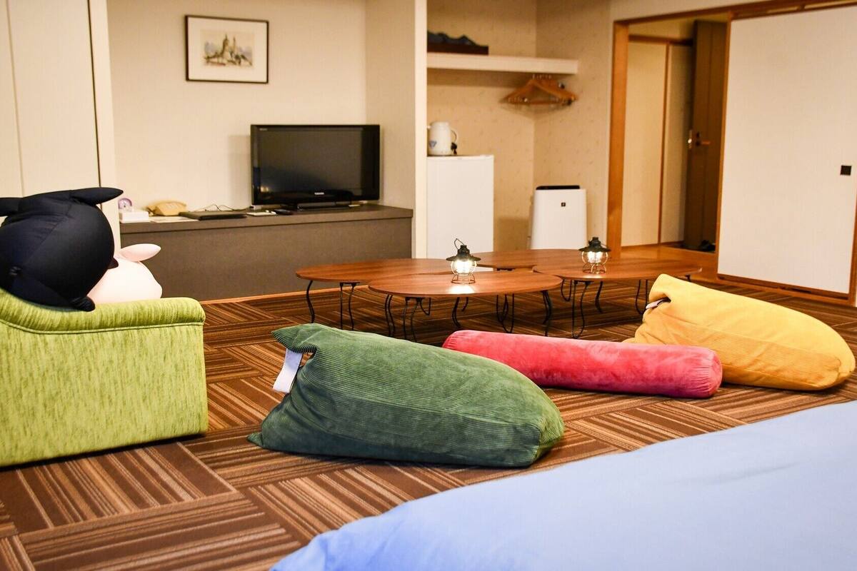 Une chambre d’hôtel avec un canapé vert, une table de salle à manger ronde accompagnée de deux chaises, une télévision et un petit coin cuisine.