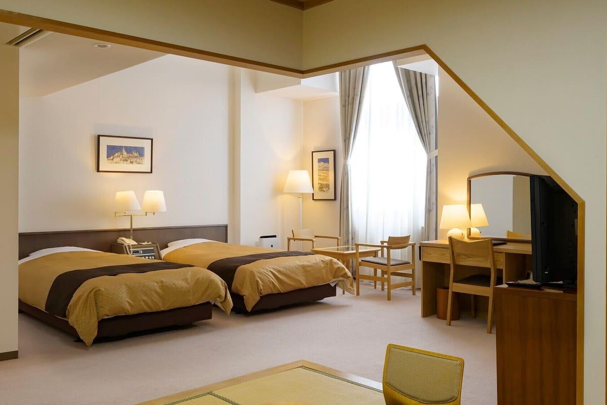 Une chambre d’hôtel avec deux lits, un bureau, une chaise, une télévision et une fenêtre avec des rideaux.