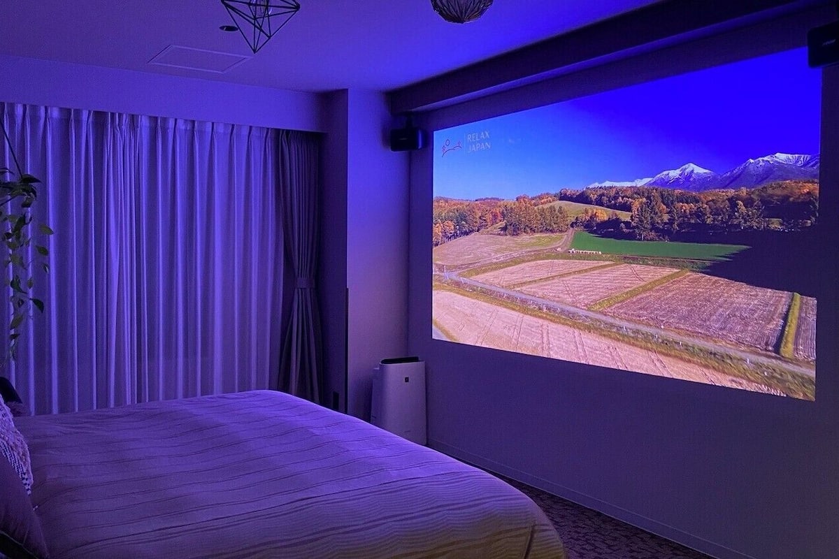 Une chambre à coucher avec un lit, des rideaux, une plante suspendue et une grande fenêtre donnant sur un paysage.