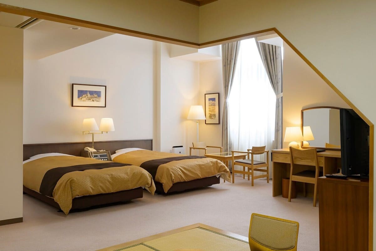 Une chambre d’hôtel avec deux lits, un bureau, une chaise, une télévision et un tableau au mur.