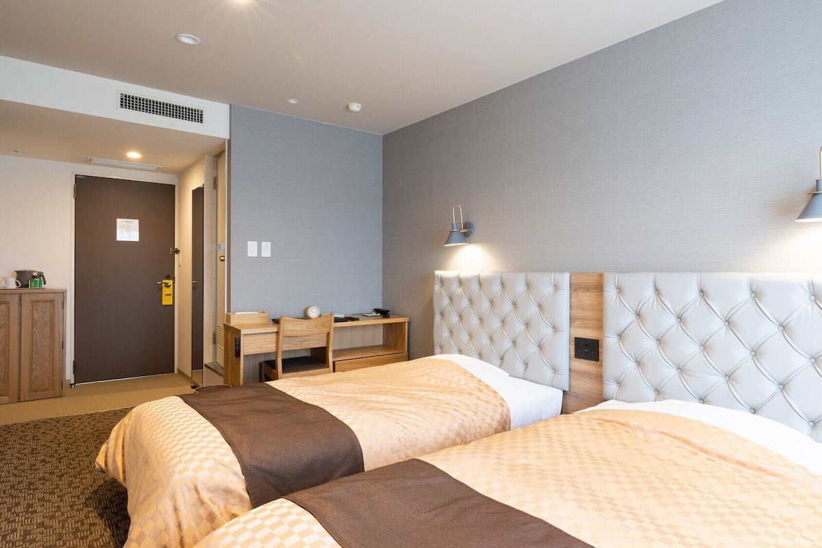 Une chambre d’hôtel avec deux lits, un bureau, une chaise et une lampe.